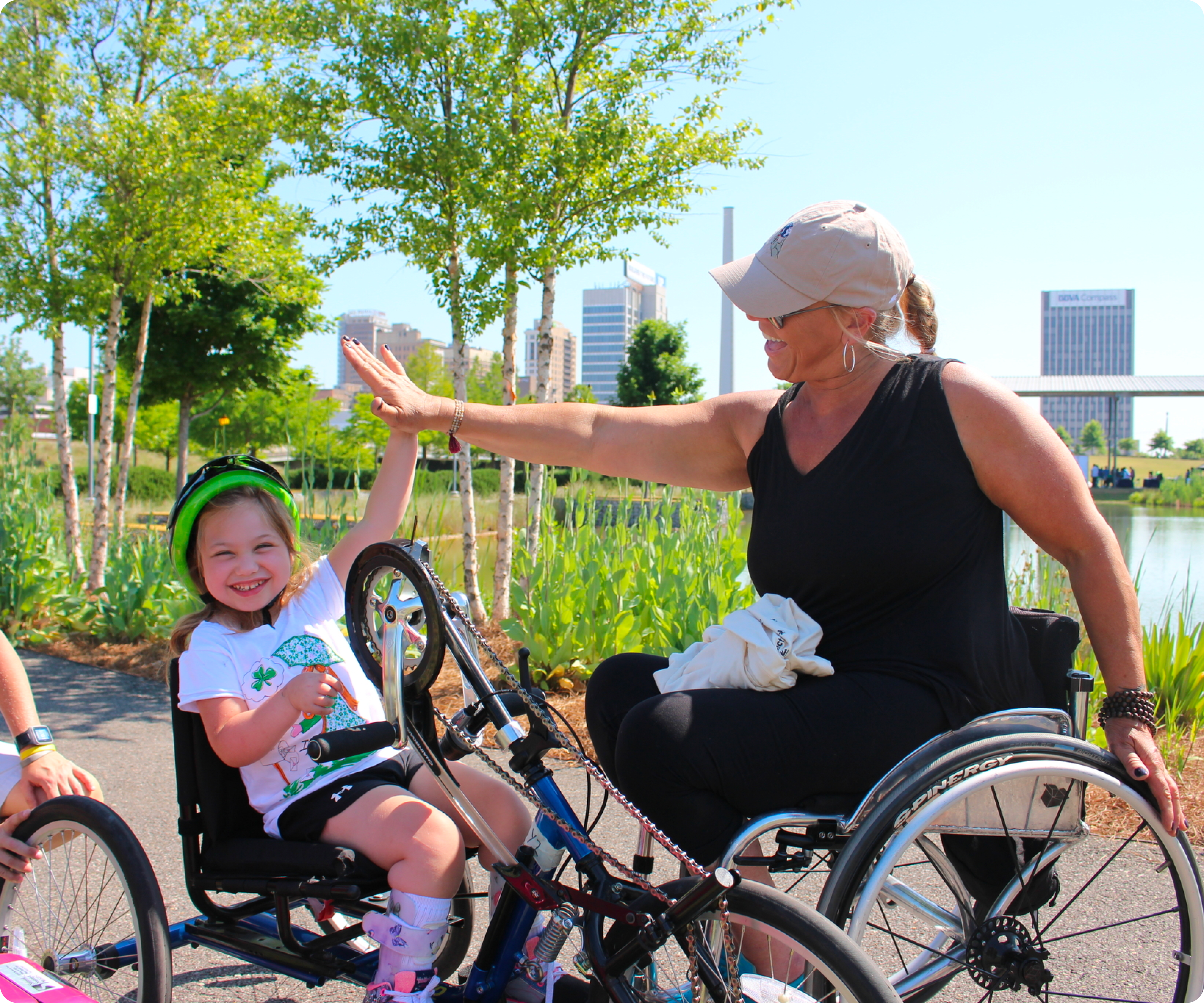 Woman in wheelchair high-fiving child with adaptive bicycle