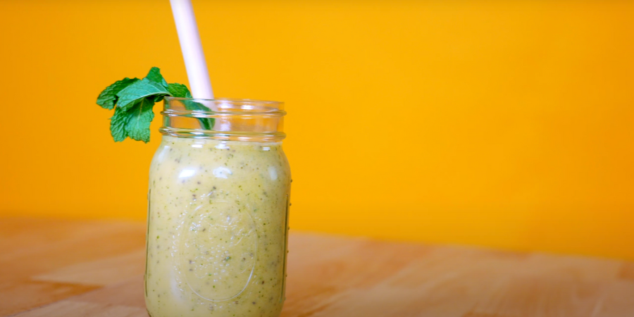 The sunshine smoothie in a glass jar with a straw and mint leaf sticking out of the top